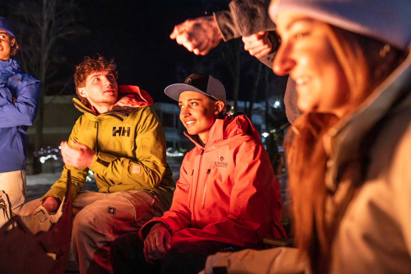 People sitting around a campfire at night, wearing winter jackets.