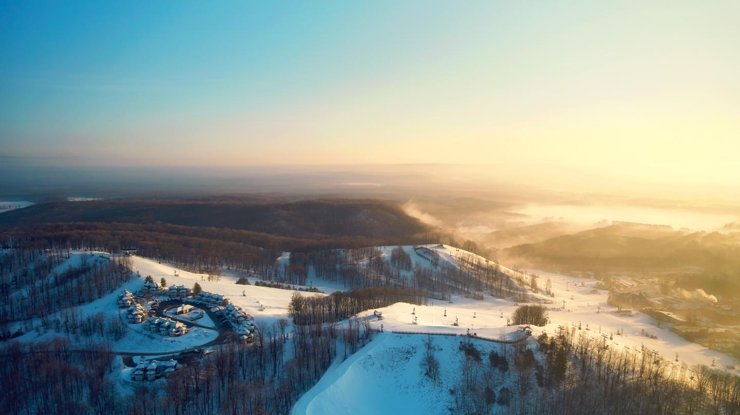 Snowy landscape at sunrise with distant hills and mist.
