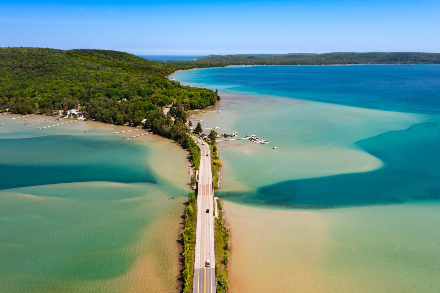 Narrow road crossing two lakes with turquoise water and lush green trees.