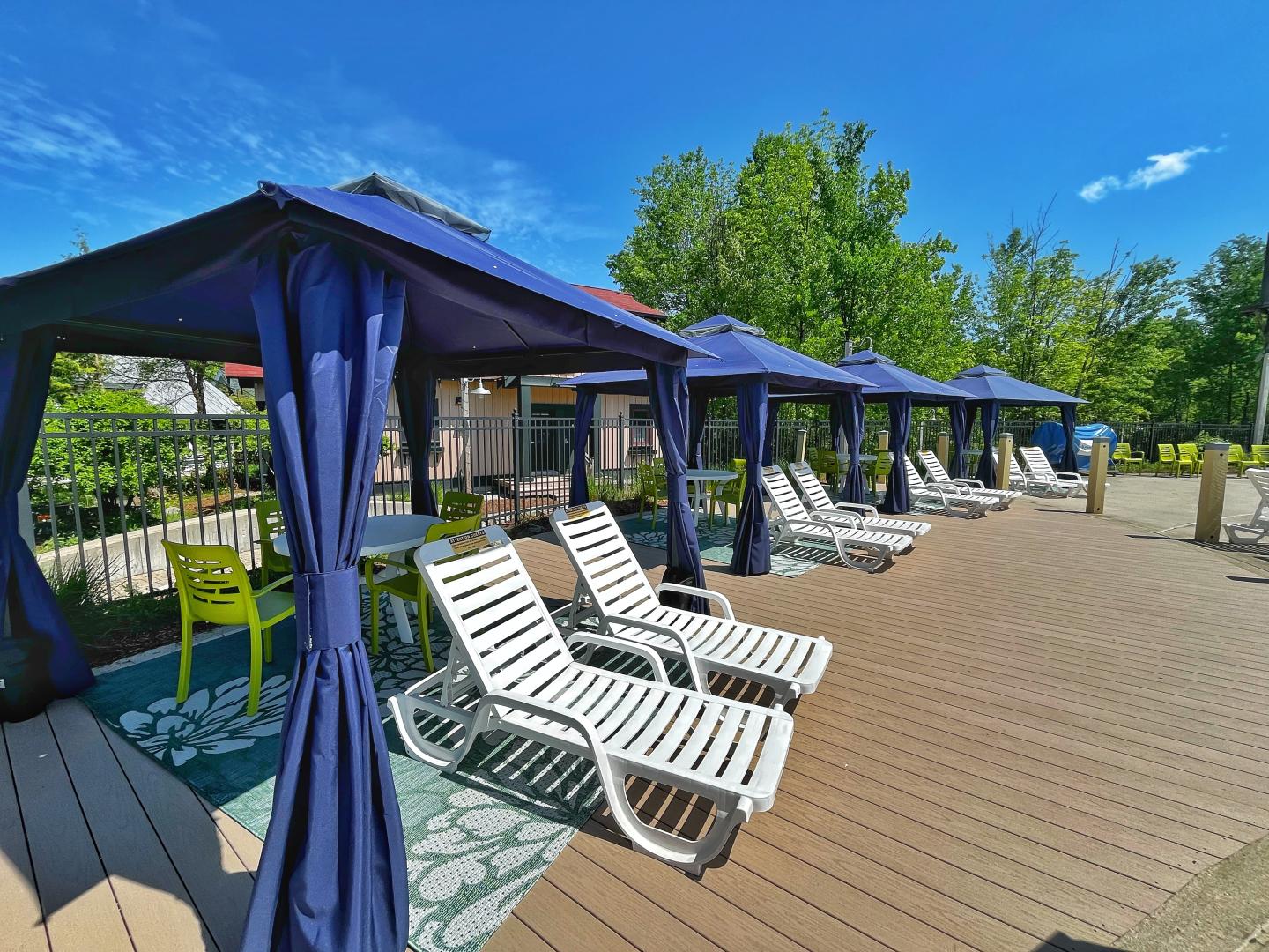 Poolside cabanas with lounge chairs, sunny weather, and green trees.