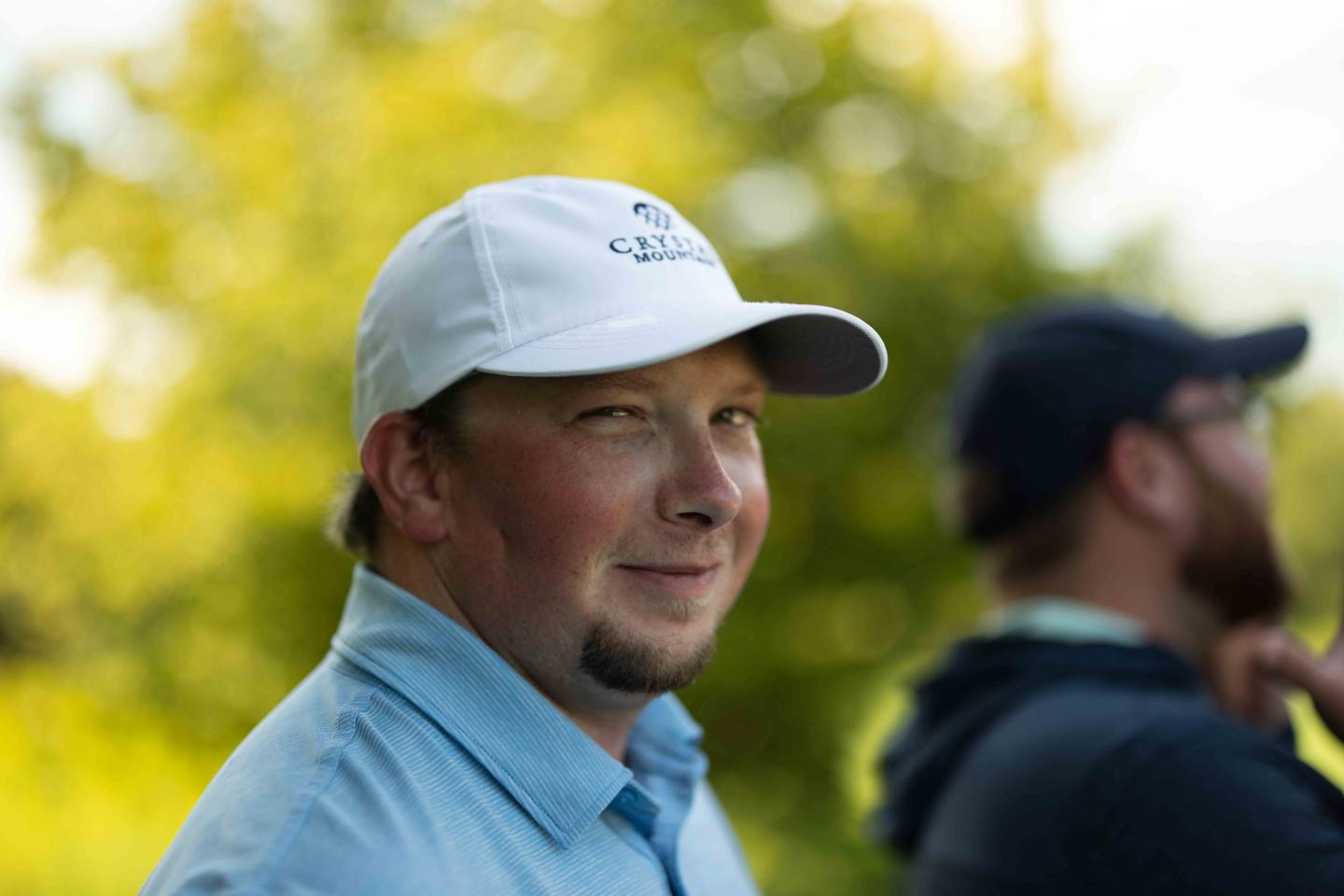 Man in a white cap smiling outdoors in soft focus background.