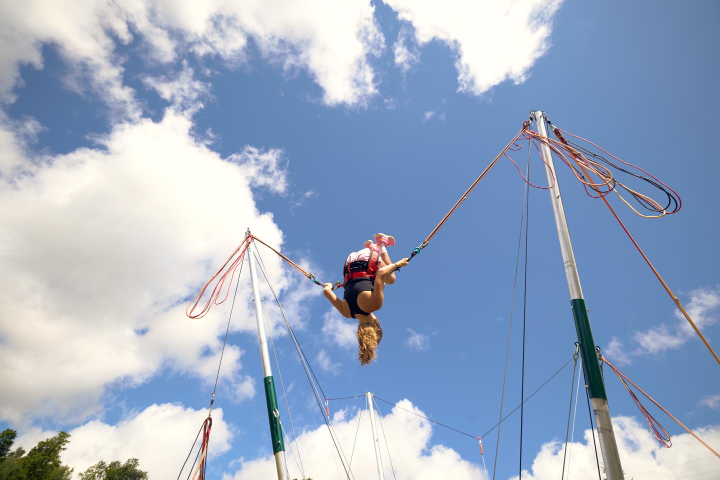 Person bungee jumping mid-air against a bright blue sky with clouds.
