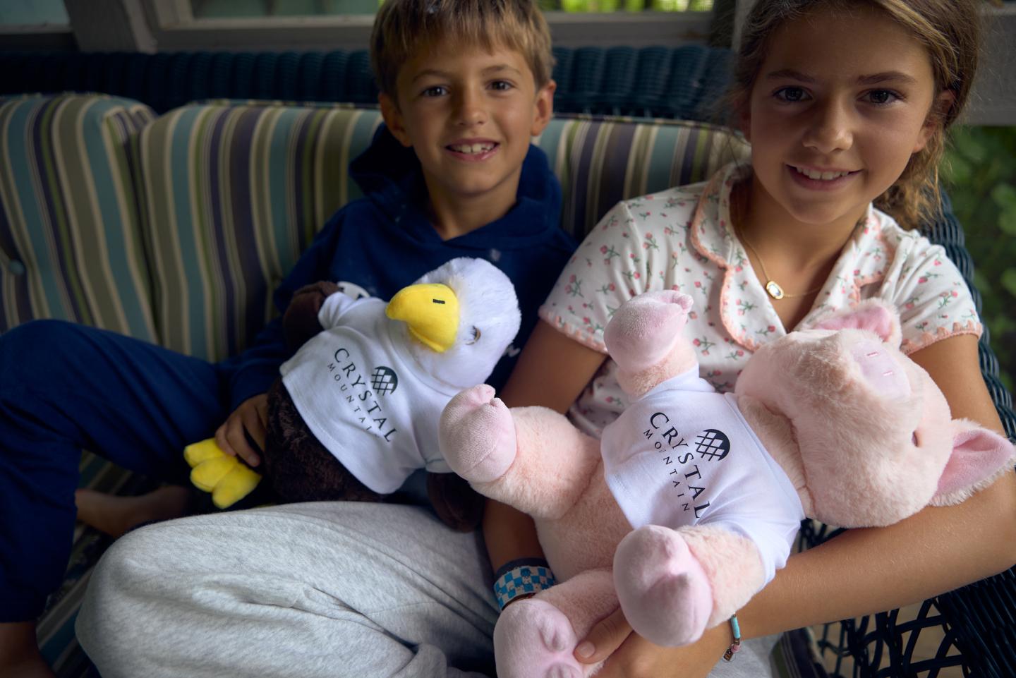 Young boy and girl on a sofa holding stuffed toys, smiling.