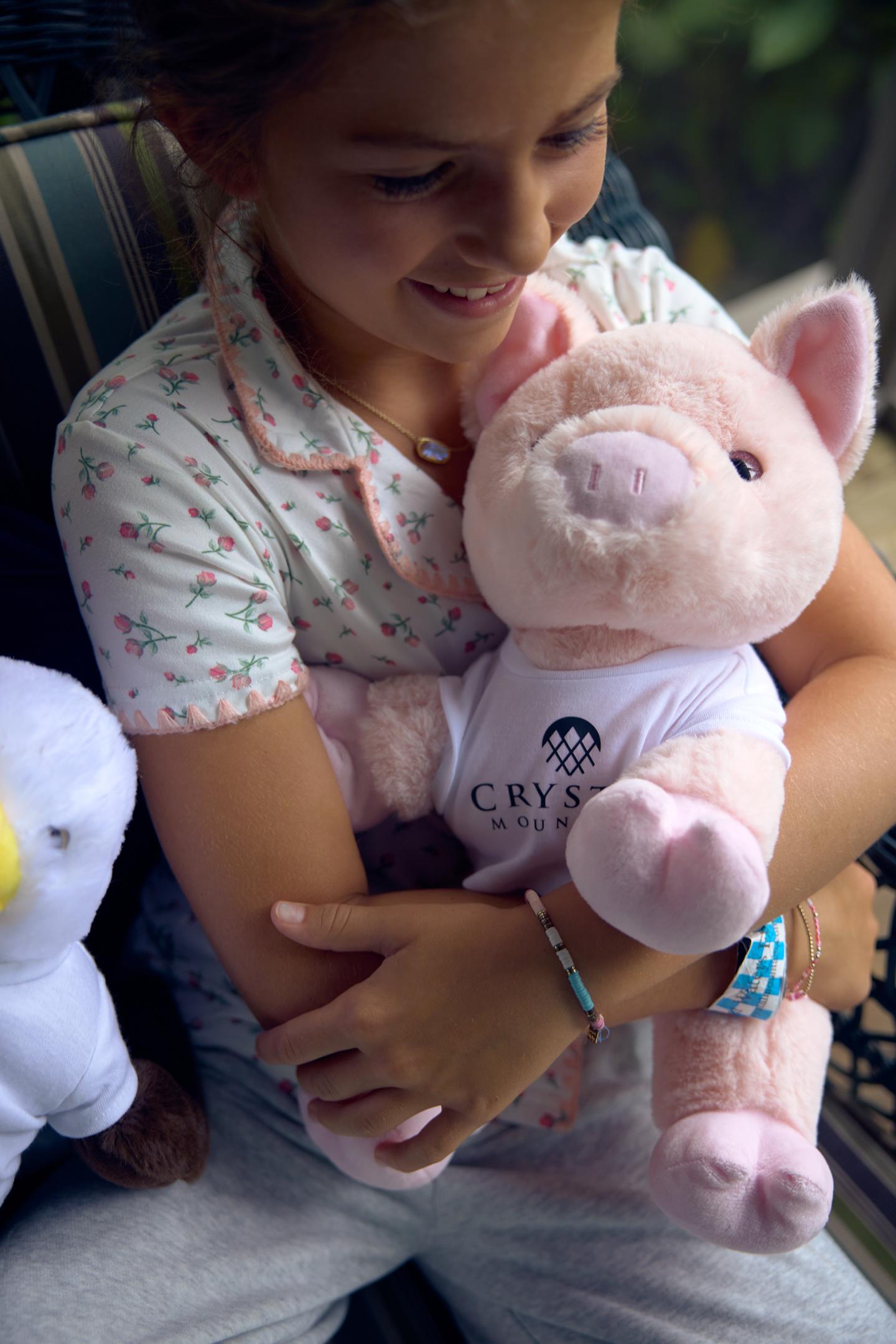 Child happily hugging a plush pig toy on a striped chair.