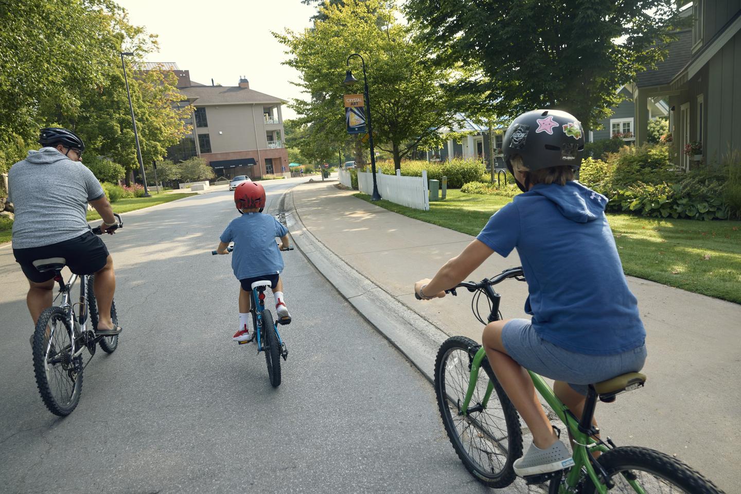Three people cycling on a neighborhood street, wearing helmets.