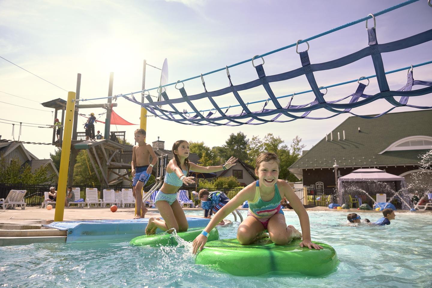 Children playing on lily pads in a sunny water park pool.