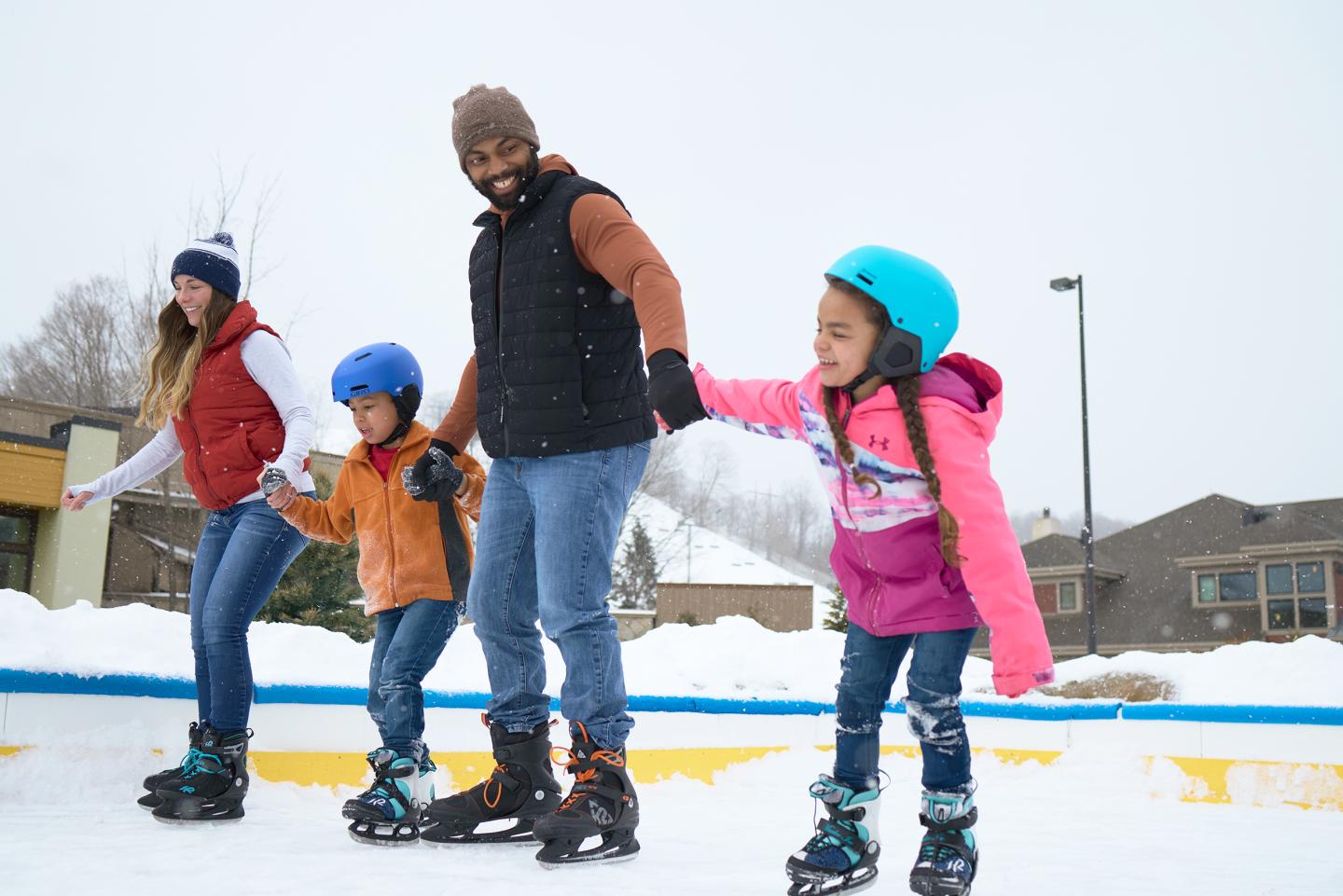 Family ice skating outdoors, smiling and holding hands.