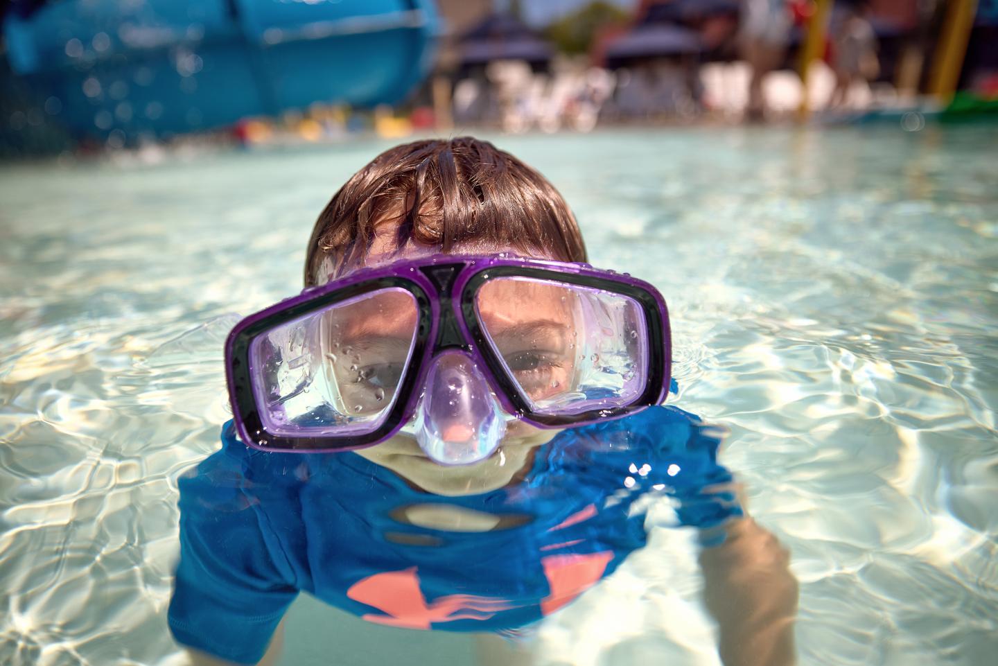 Child in goggles swimming in a pool, smiling.