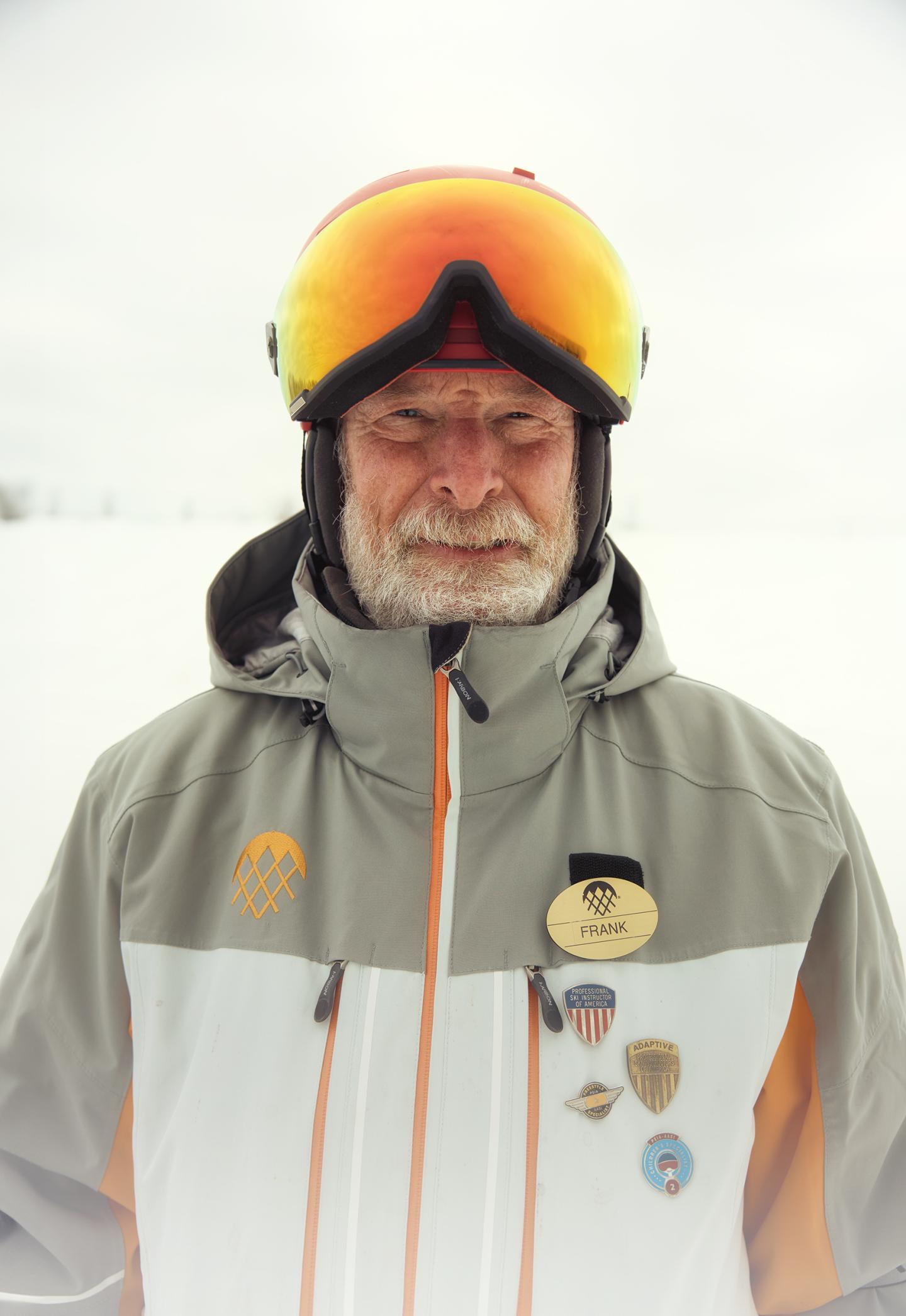 Elderly man in ski gear with medals, eyes closed, snowy background.
