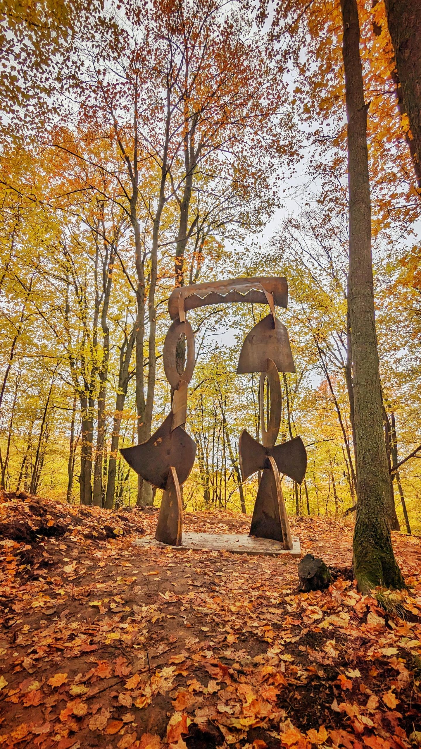 Wooden sculpture in autumn forest with colorful leaves.