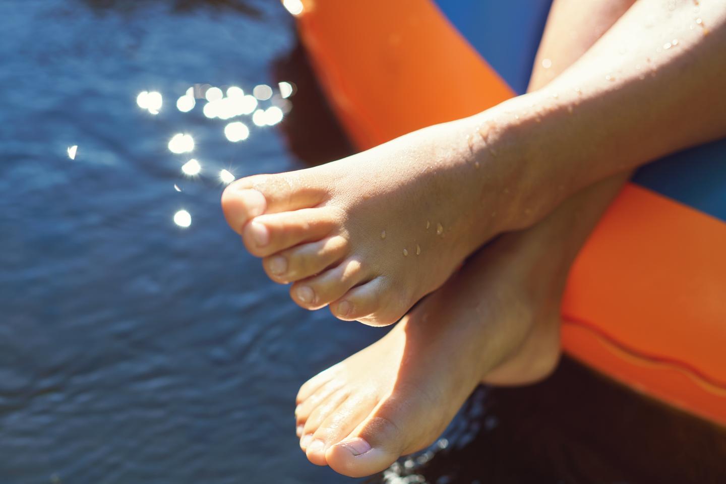 Feet resting on an orange inflatable in the water, sunlight sparkling on the surface.