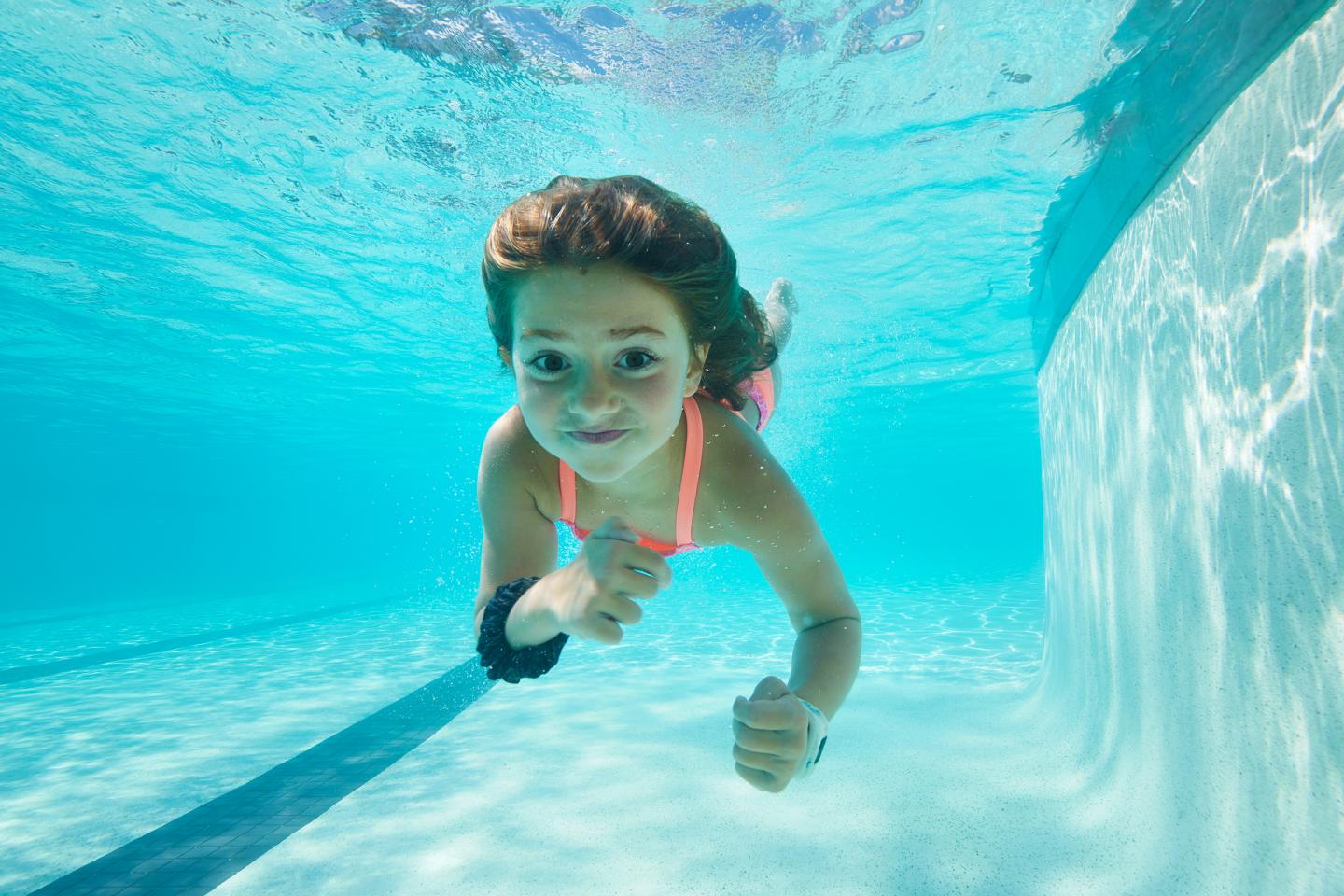 Girl swimming underwater in a pool, wearing a pink swimsuit.
