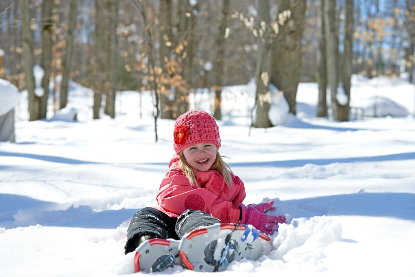 Child in pink playing in snow, surrounded by trees.