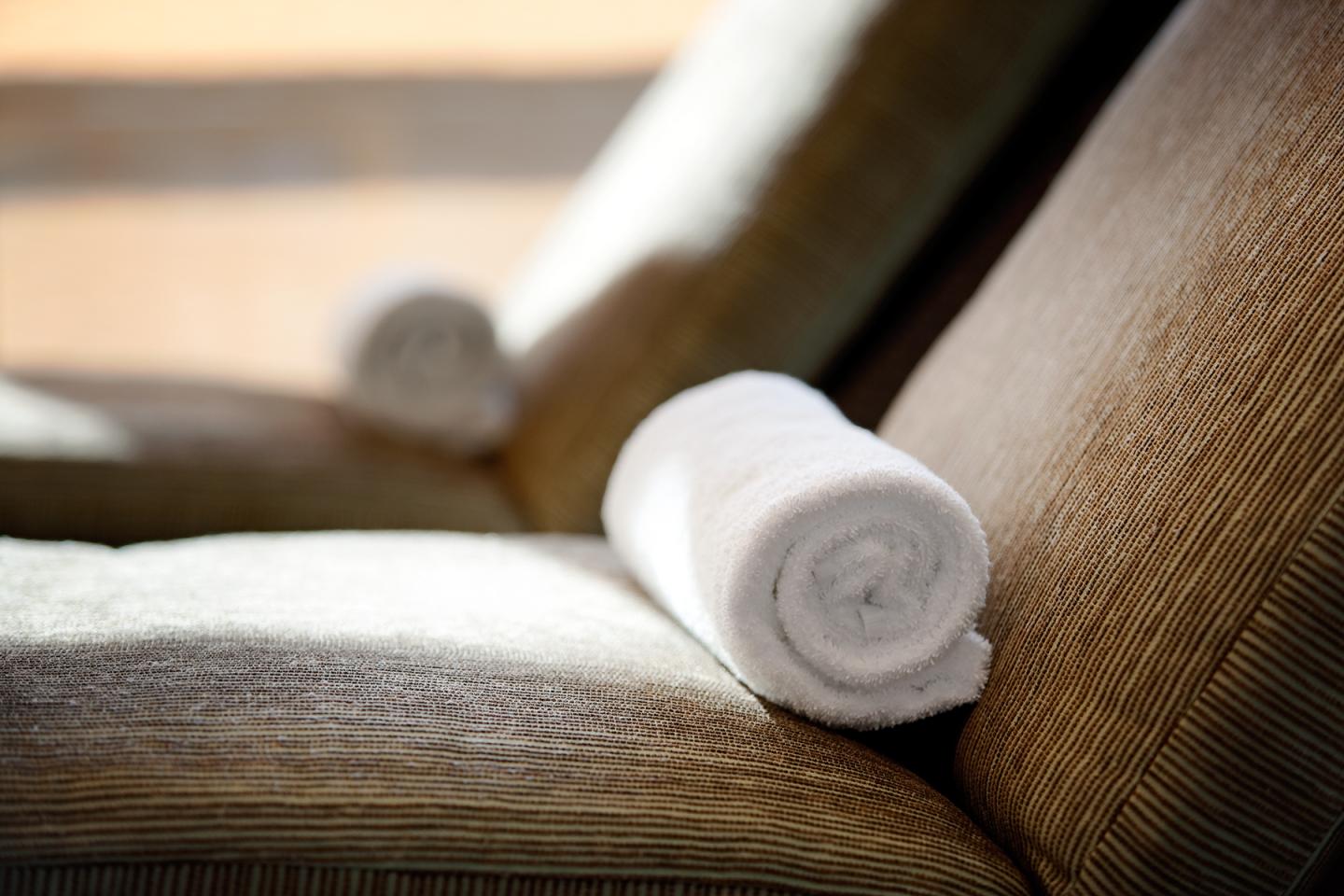 Rolled white towels on a spa chair, sunlight streaming in.