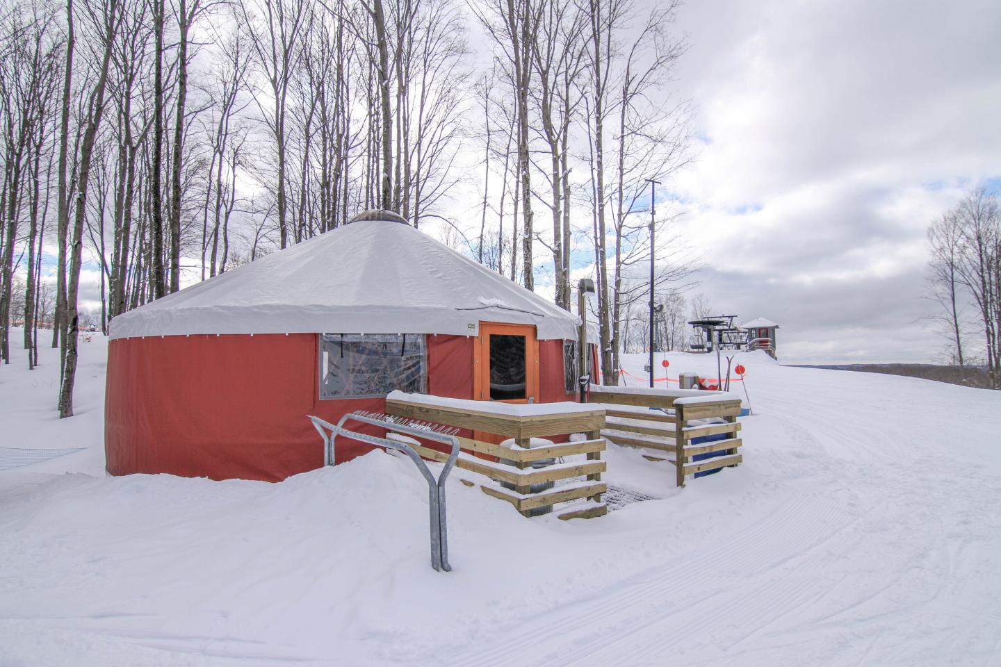Red yurt in snowy landscape with leafless trees and cloudy sky.