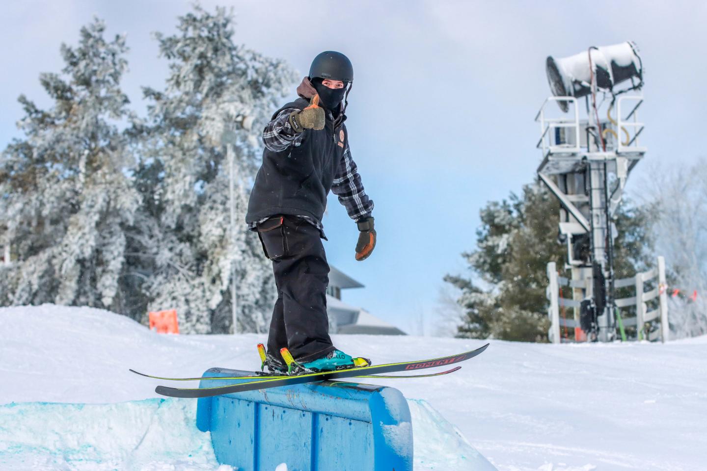 Skier balancing on rail in snowy landscape, wearing black gear and helmet.