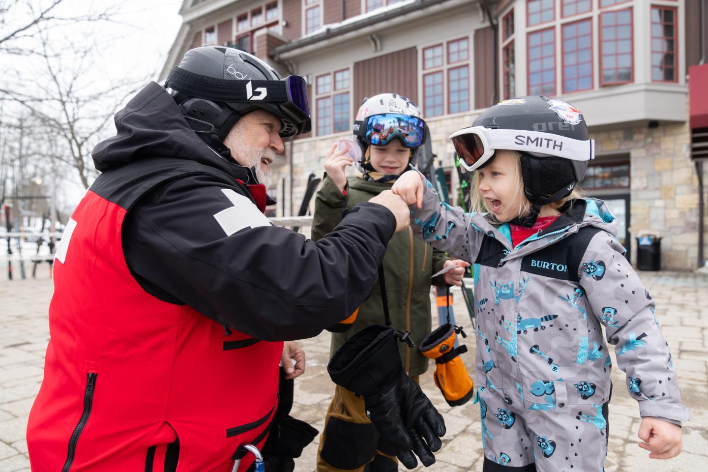 Ski patroller fist-bumps a smiling child in ski gear outside Kinlochen.
