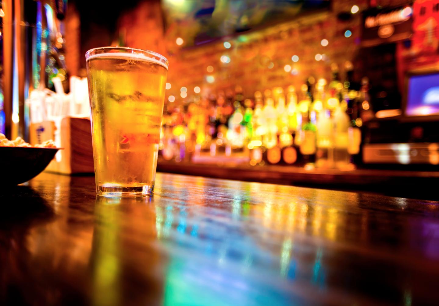 A pint of beer on a bar counter, with colorful lights in the background.