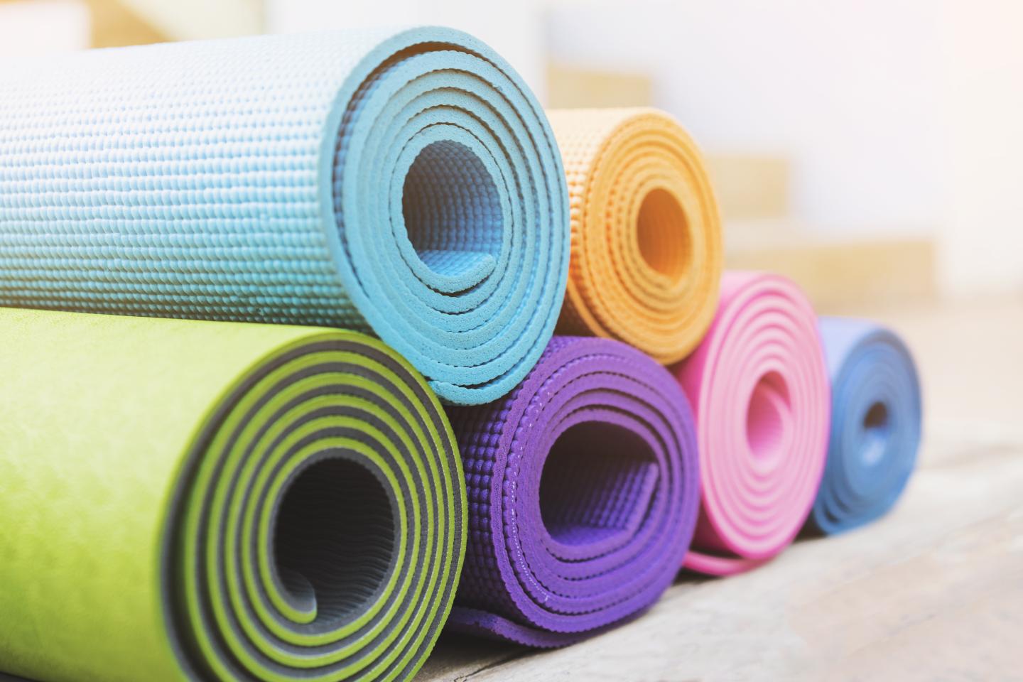 Rolled yoga mats in various colors stacked together.
