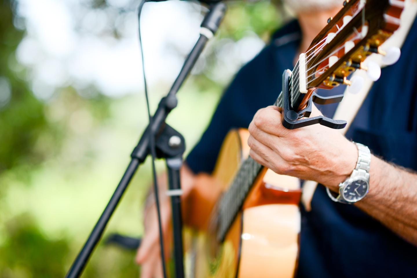 Man playing an acoustic guitar near a microphone outdoors.