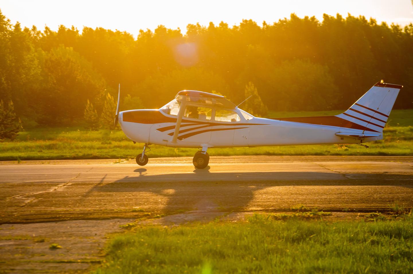 Small airplane on runway at sunset with trees in background.