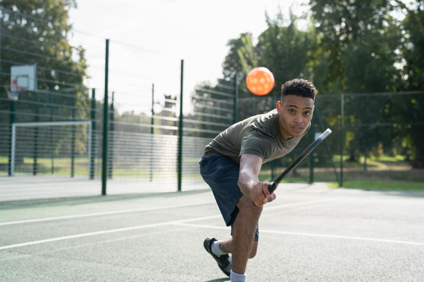 Man playing pickleball outdoors, reaching with paddle for an incoming ball.