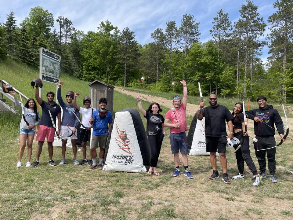 Group with bows standing outside near trees and targets, smiling and posing energetically.