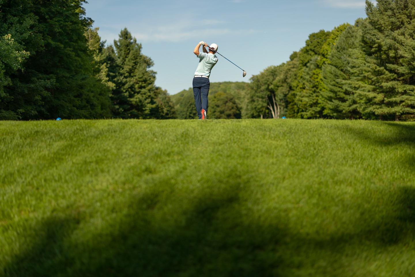 Golfer swinging on a lush, green course surrounded by trees.
