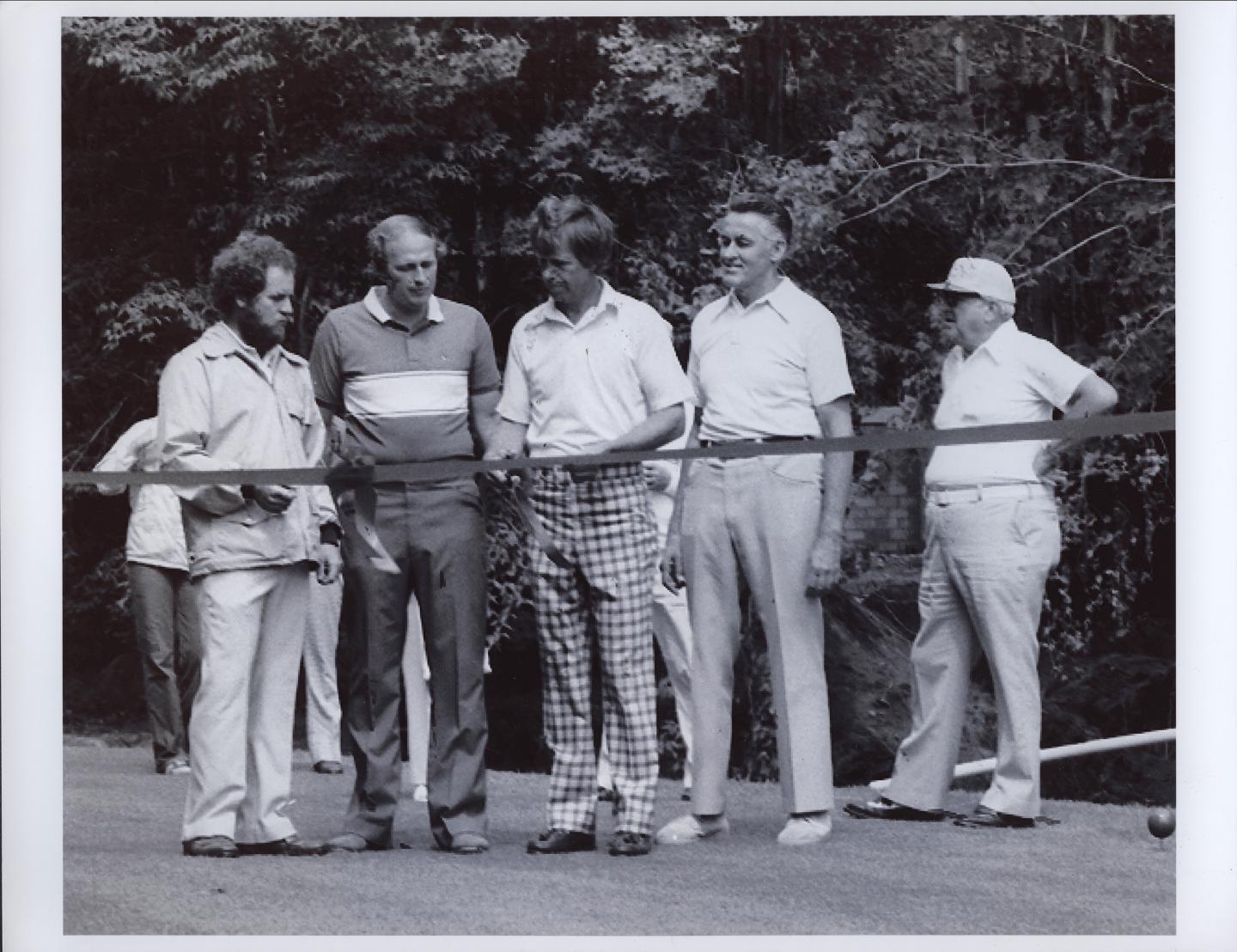 Five men standing outdoors in casual attire, at a ribbon cutting ceremony.
