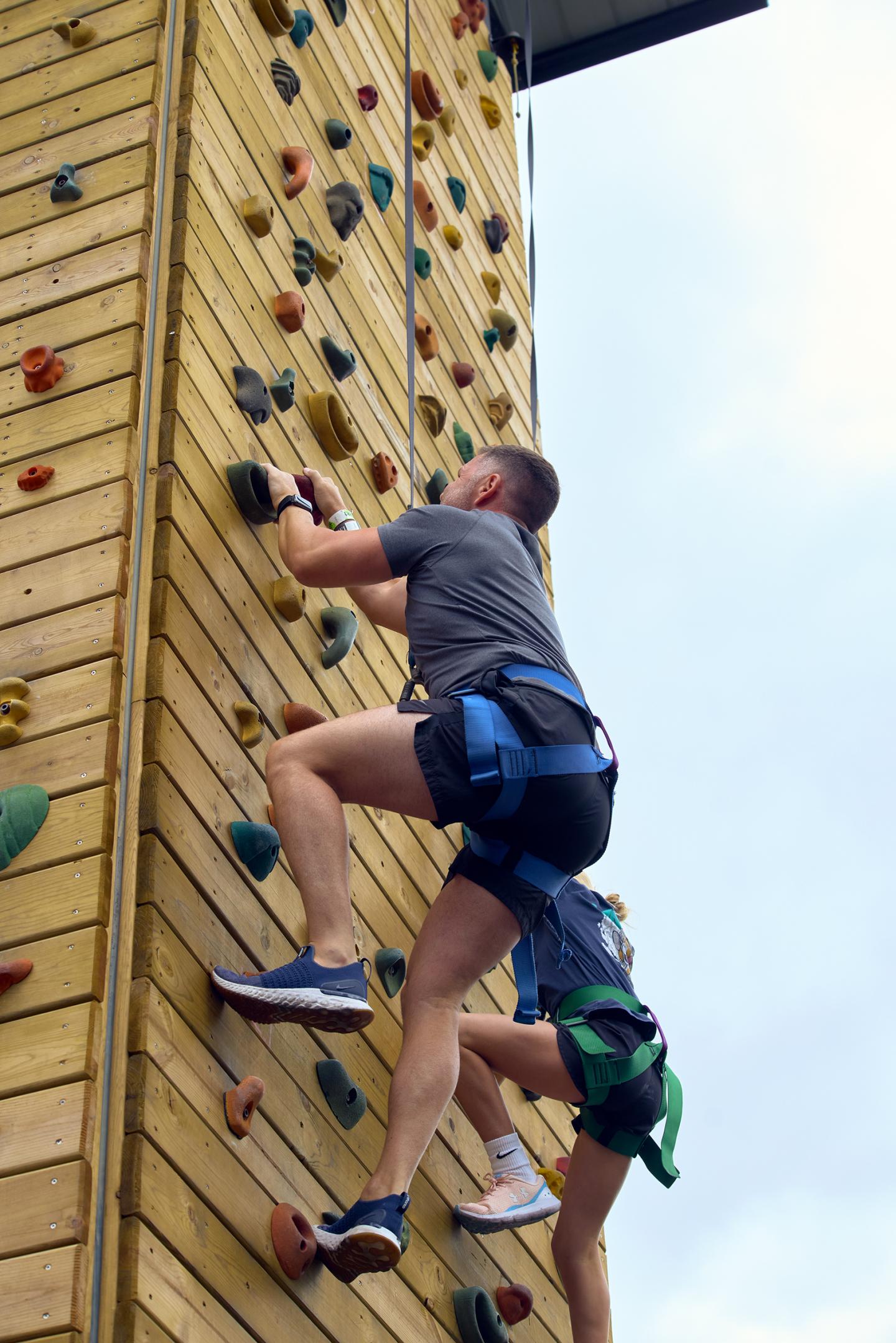 Two people climbing an outdoor wooden rock wall.