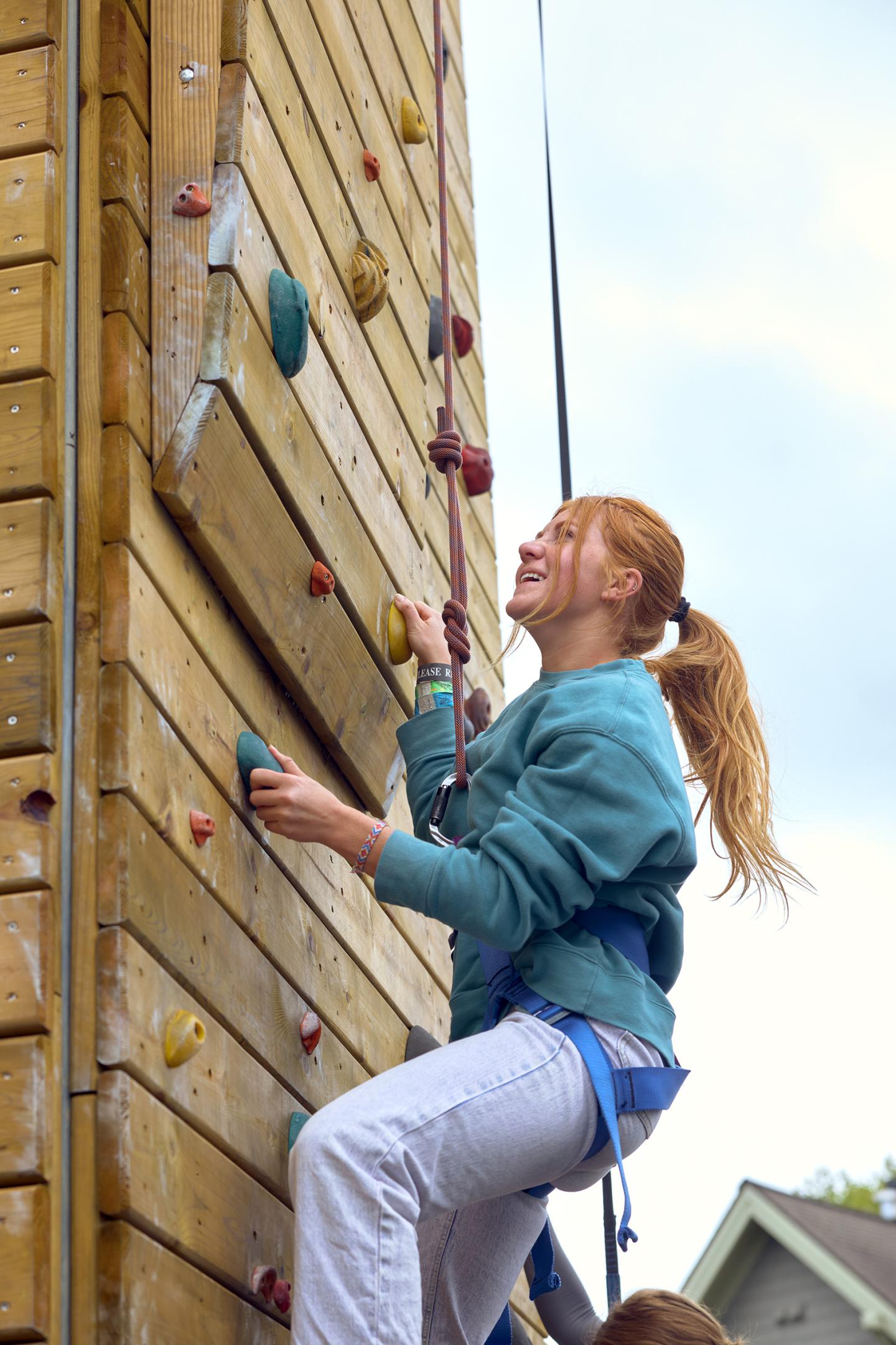 Woman climbing outdoor rock wall, smiling, wearing harness.