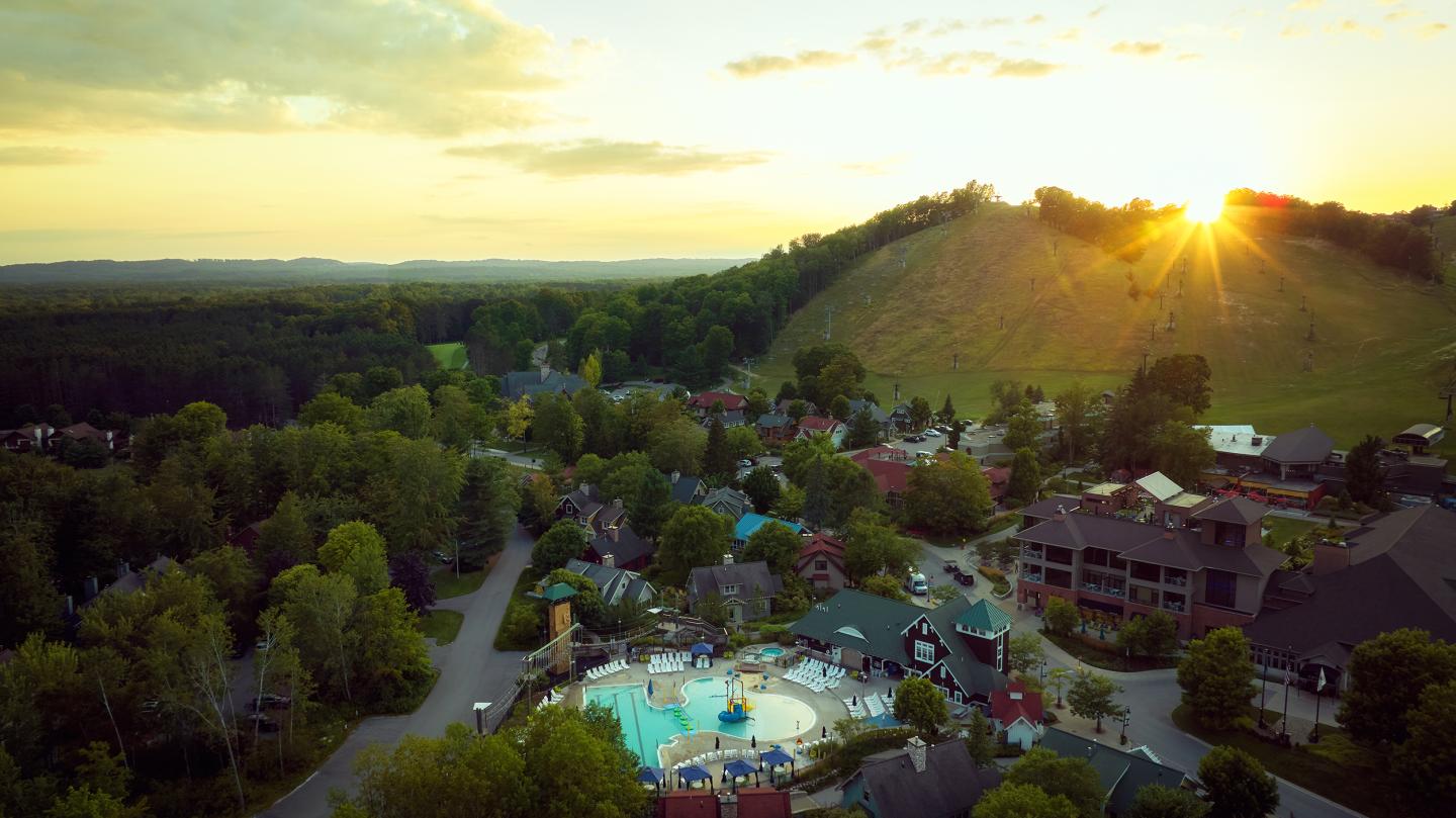 Rural landscape at sunset with hills, trees, and buildings.
