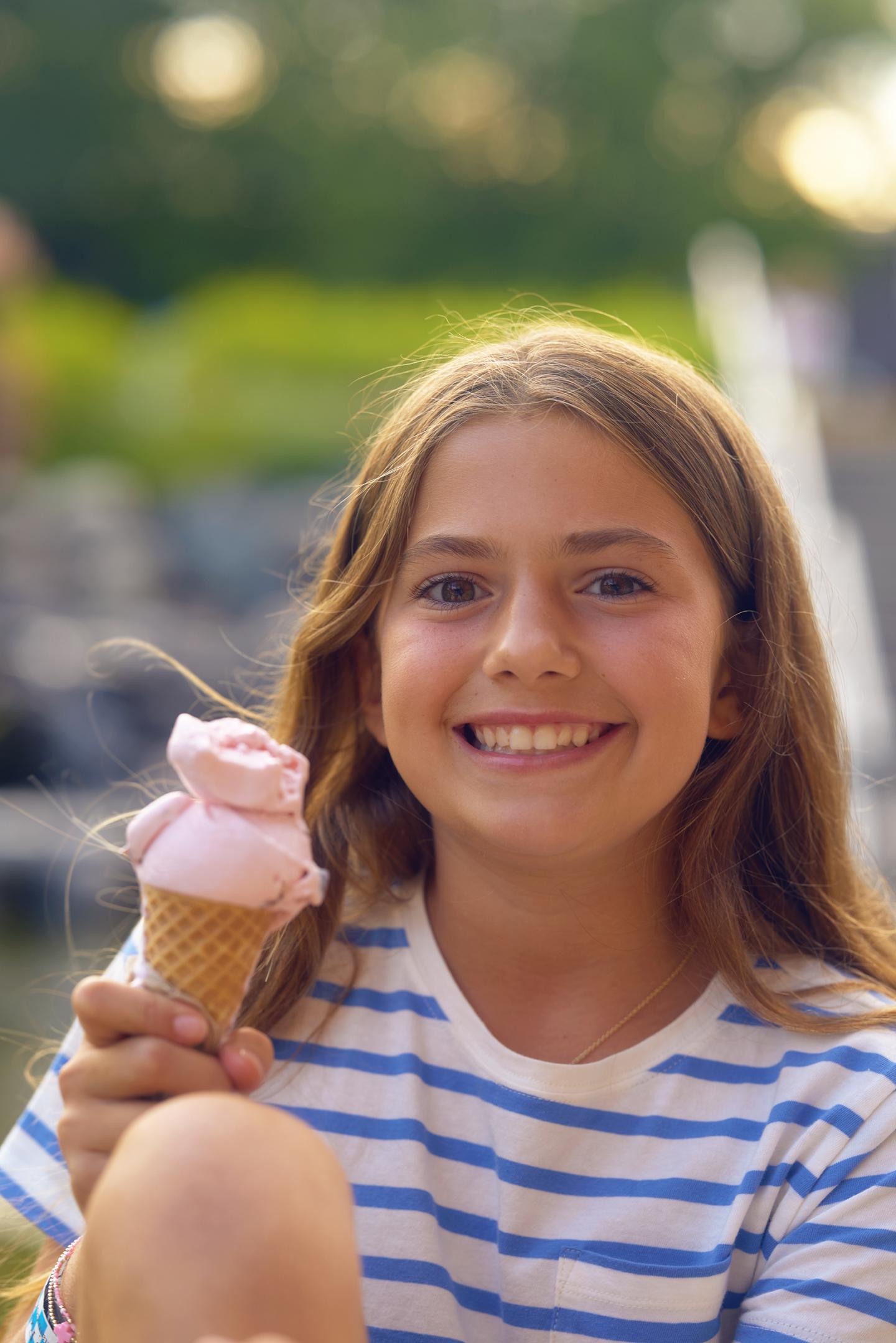 Girl smiling outdoors holding a pink ice cream cone.