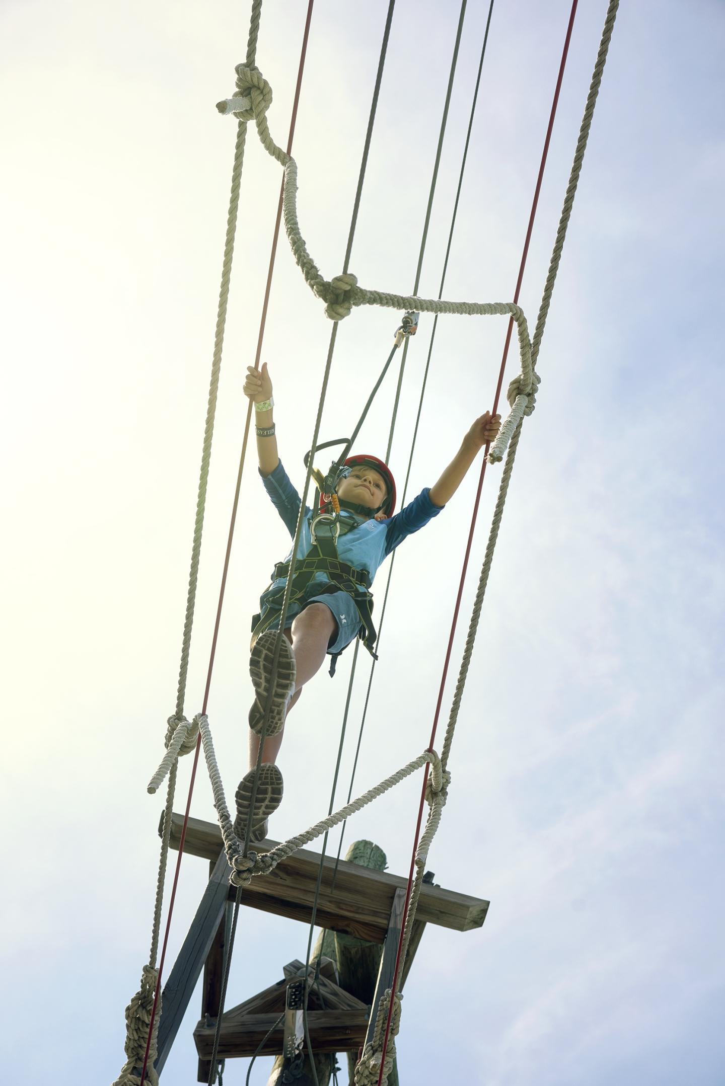 Person balancing on a high ropes course, wearing a harness and helmet.