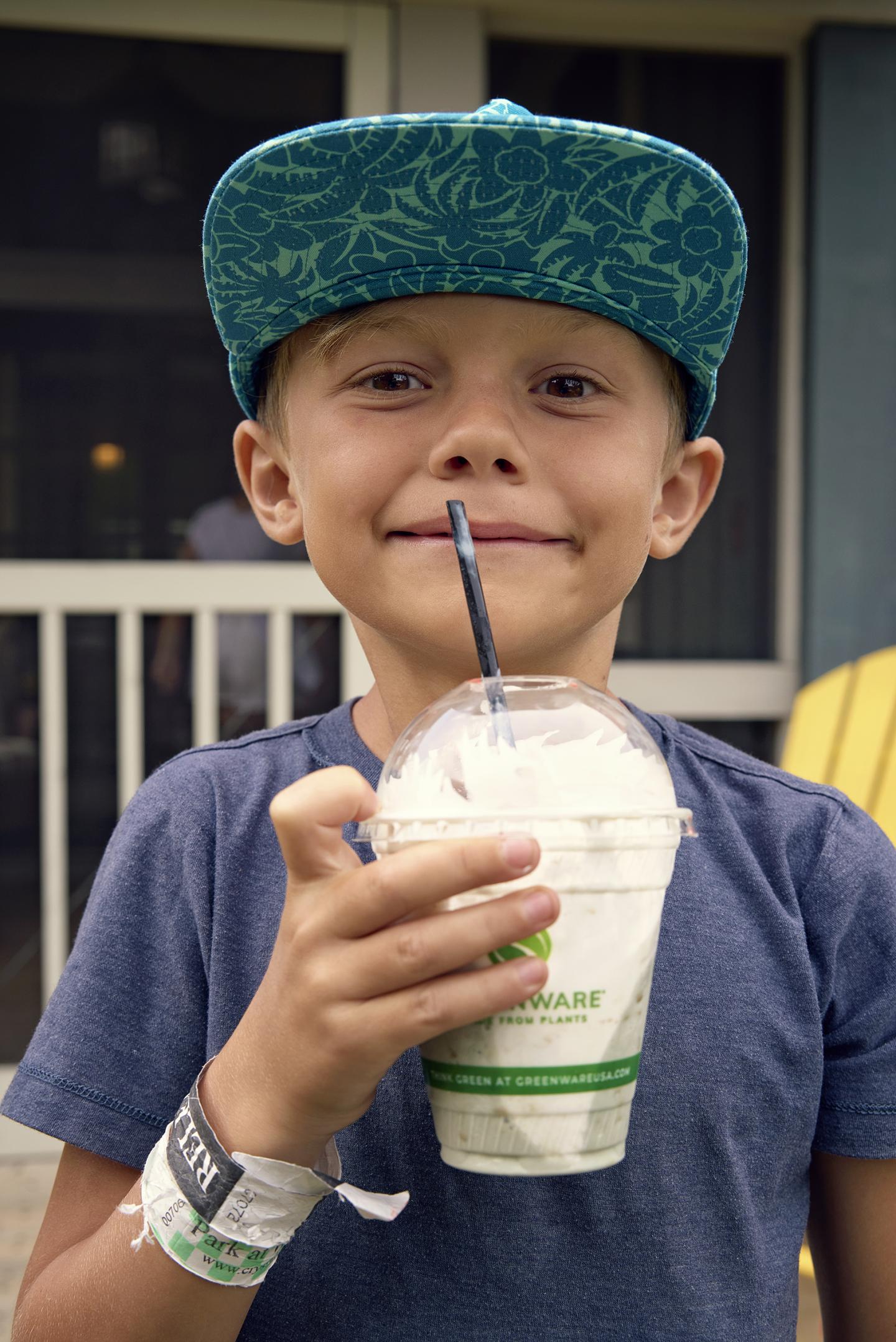 Young boy with a blue cap holding a smoothie and smiling.