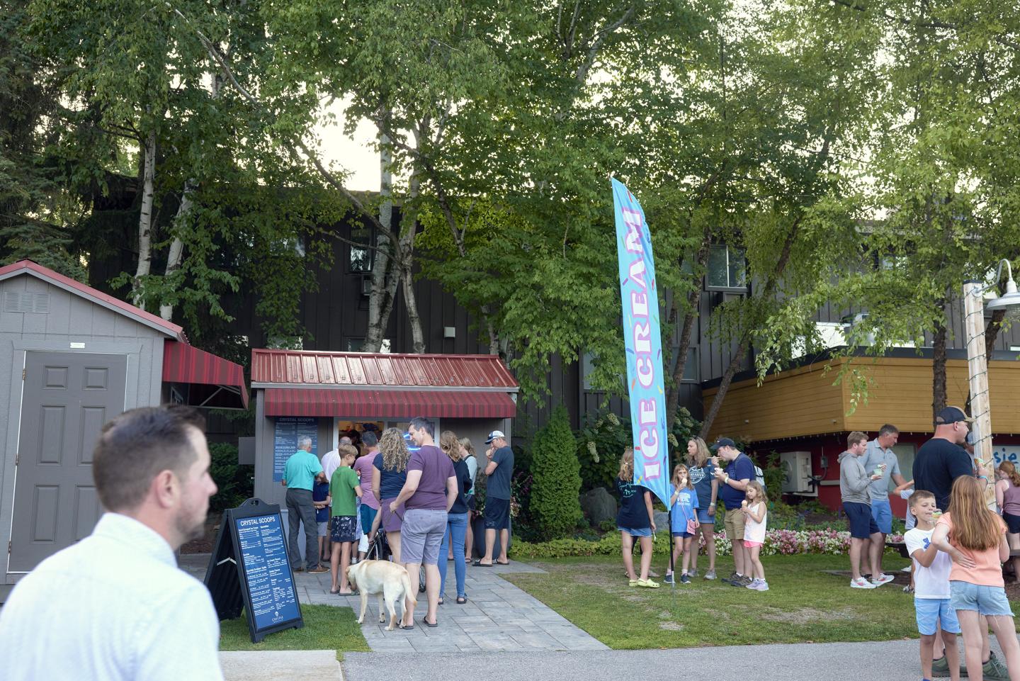 Crowd outside an ice cream stand with trees in the background.