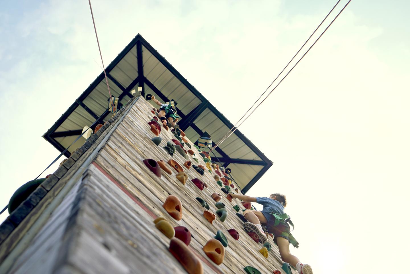 Climber scaling a tall outdoor climbing wall under a clear sky