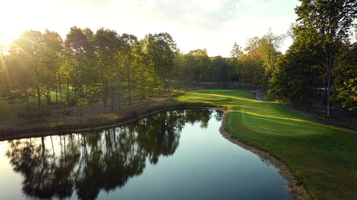 Golf course with pond, surrounded by trees in soft sunset light.
