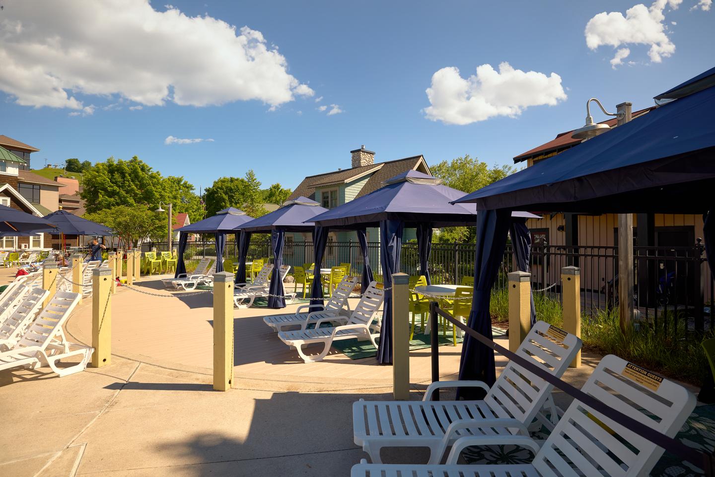 Poolside loungers under blue canopies on a sunny day.