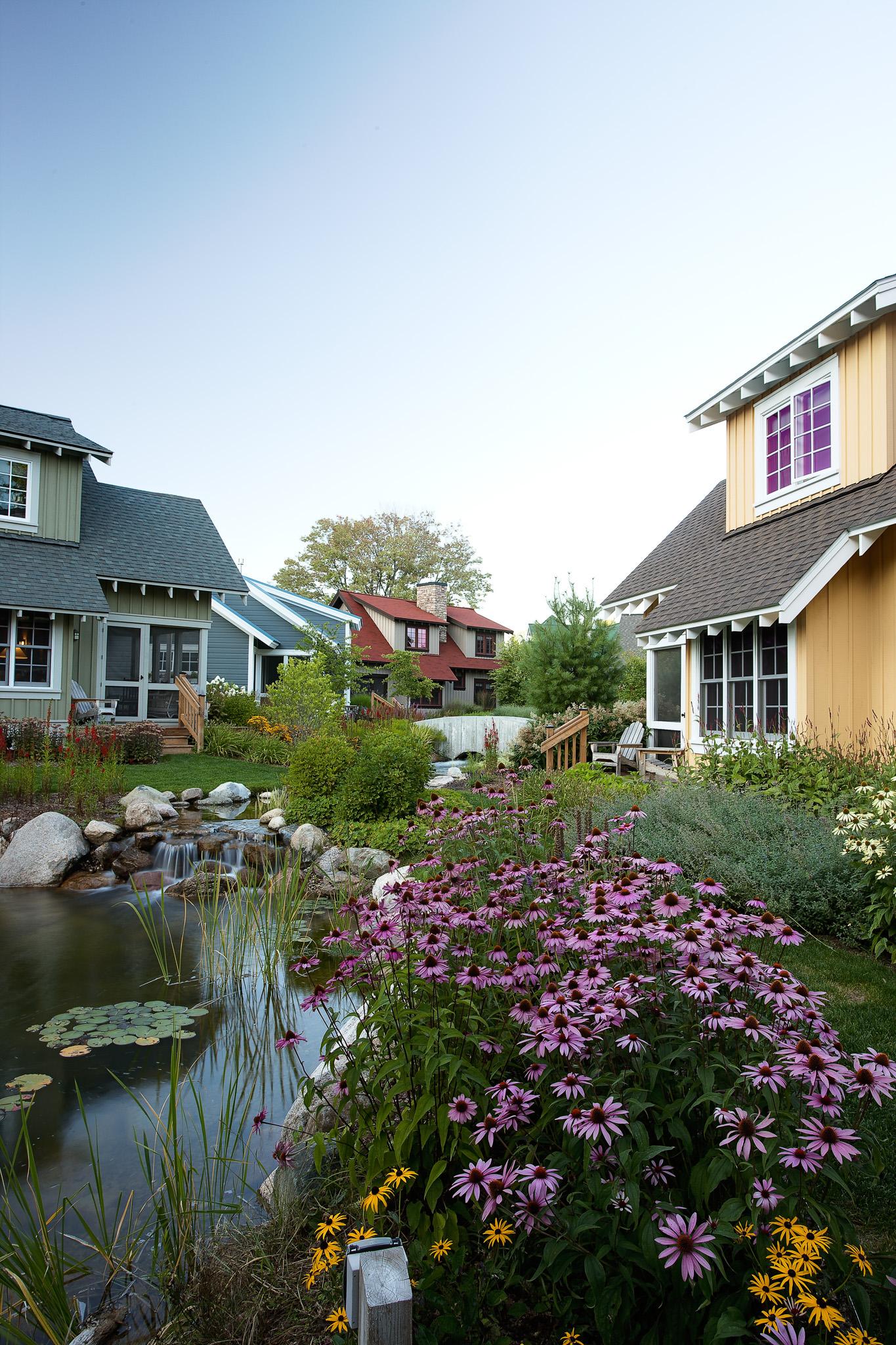 Colorful houses with blooming garden by a pond under a clear sky.