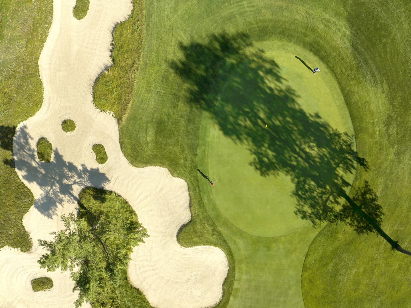 Golf course aerial view with sand bunkers, green, and long tree shadow.
