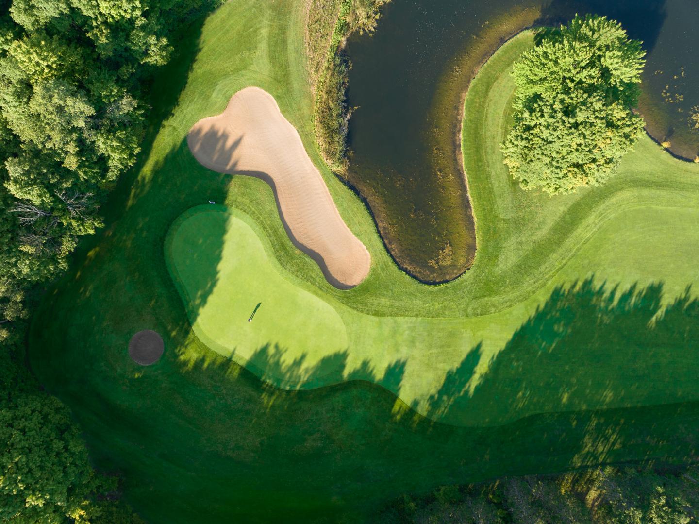 Golf course aerial view with sand trap, green, and pond.