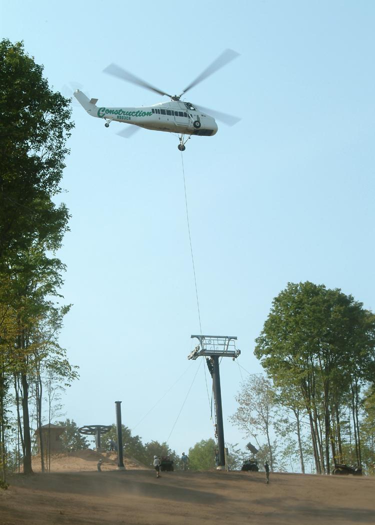 Helicopter lifting equipment near a forested area.