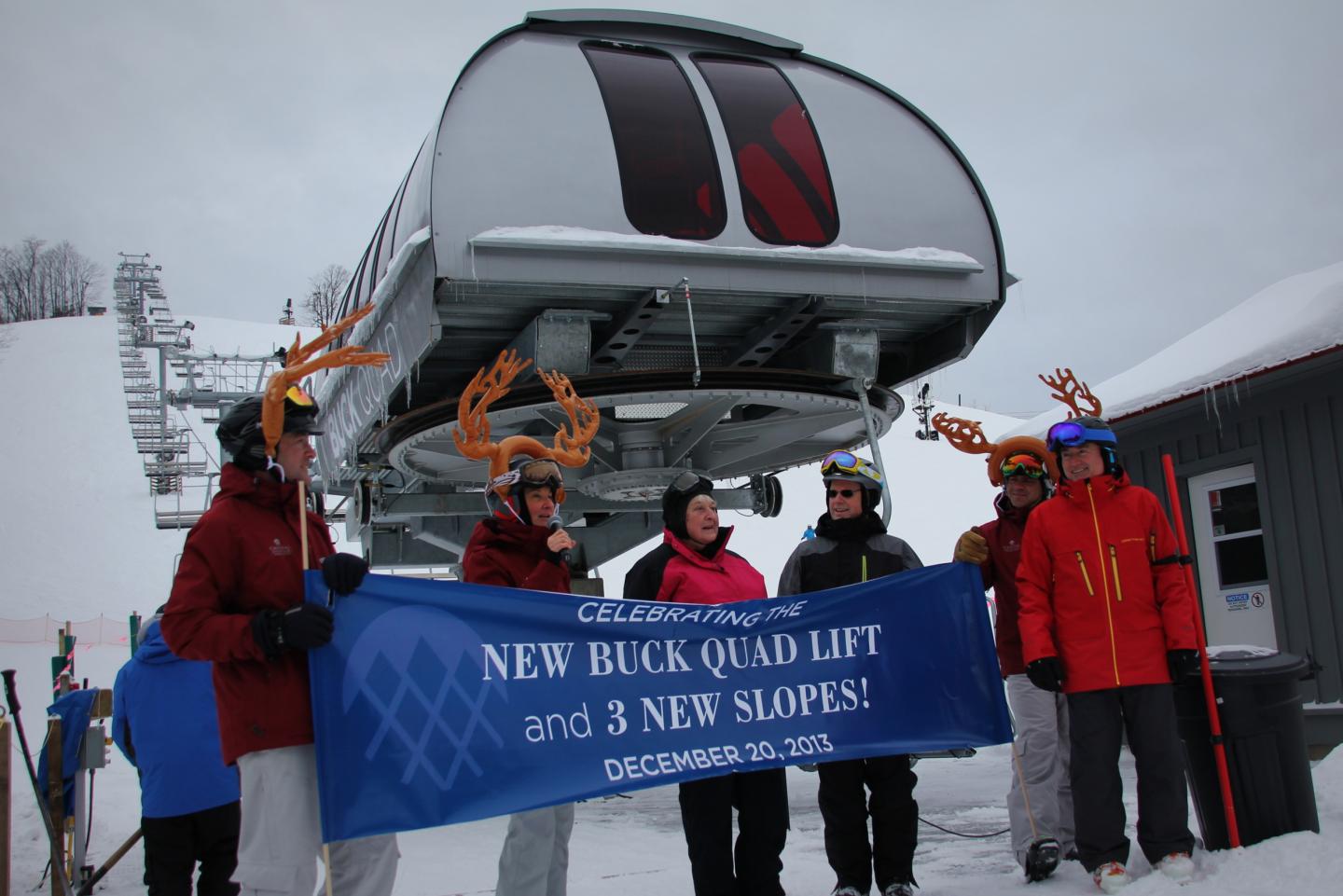 Ski lift opening event with people in winter gear holding a blue banner.