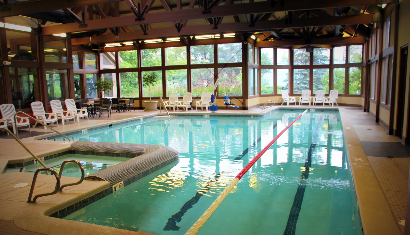 Indoor pool with lanes, surrounded by chairs and large windows. Natural light illuminates the area.