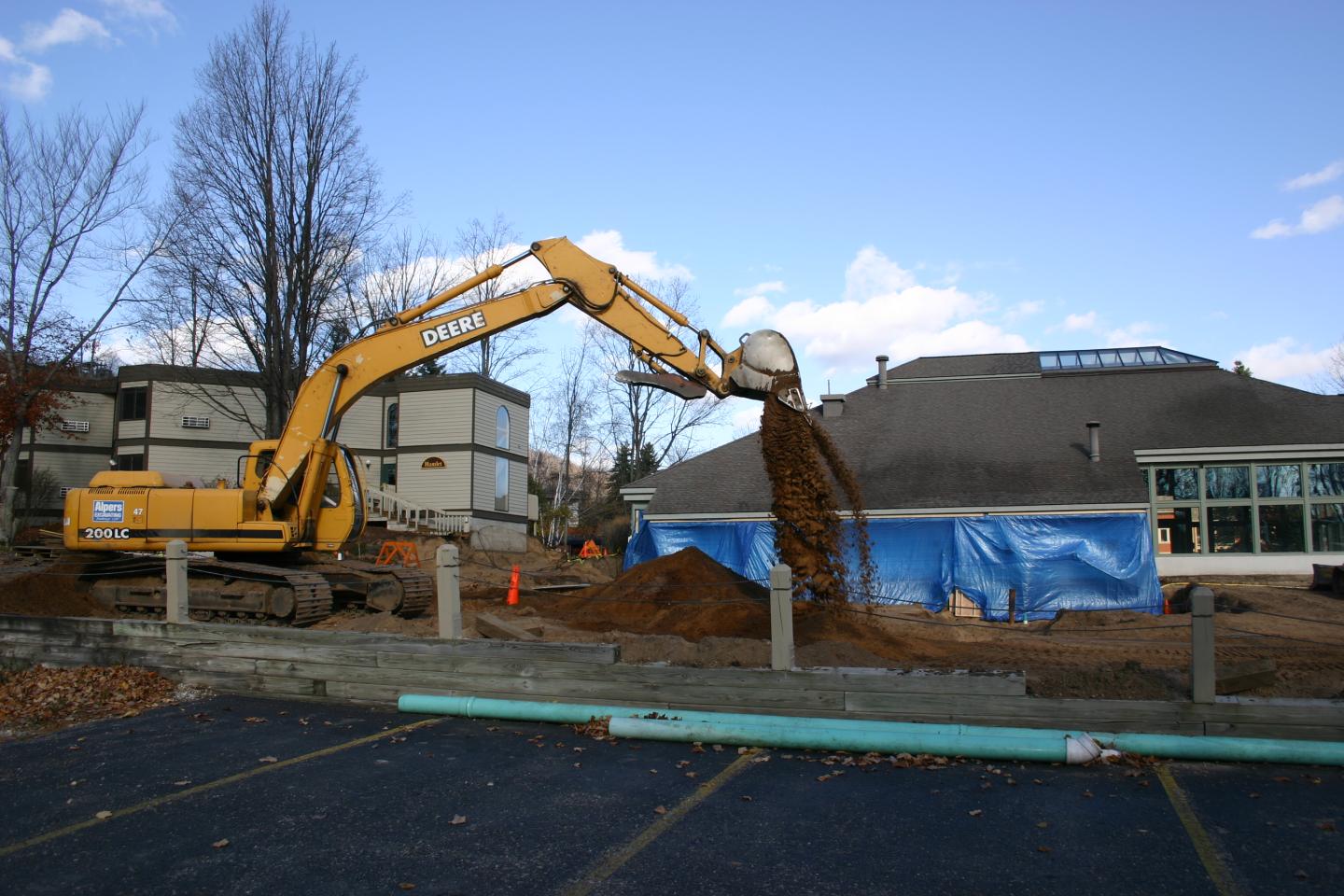 Yellow excavator moving dirt at a construction site with blue tarps.