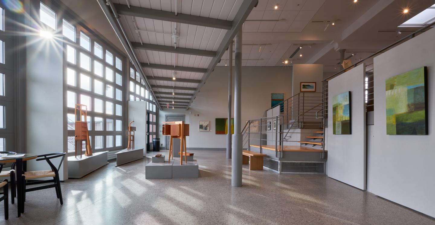 Contemporary art gallery with paintings, sculptures, and large windows.