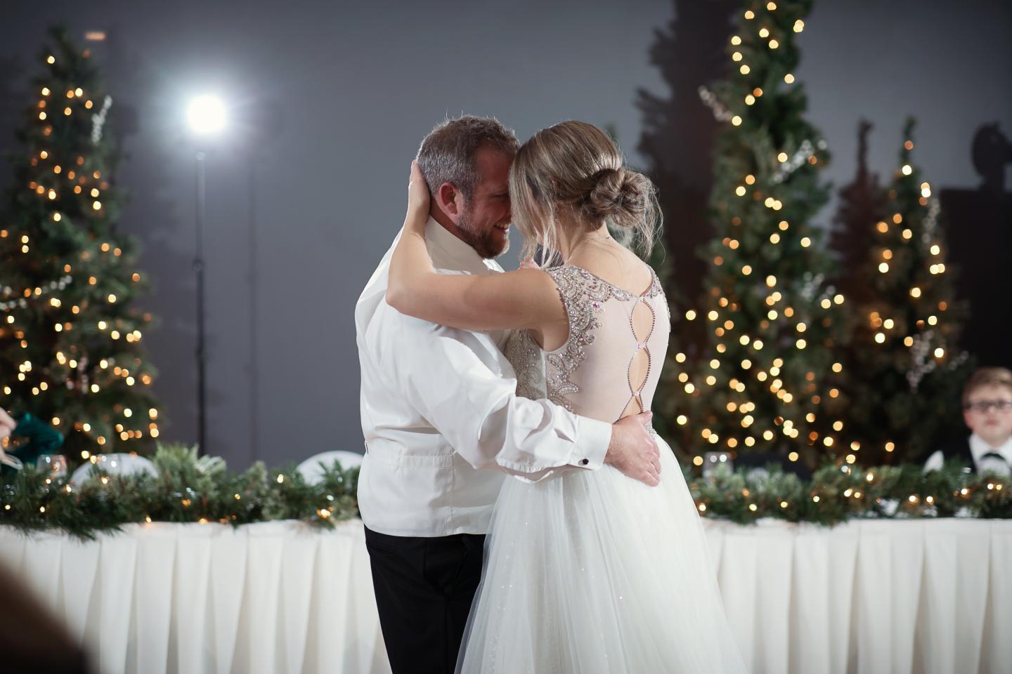 Bride and groom dancing, surrounded by lit Christmas trees.