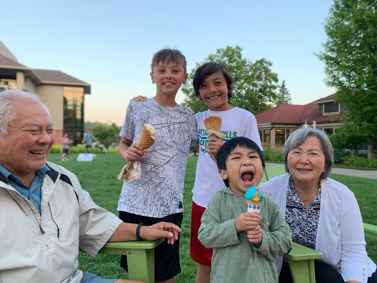 Older couple and three kids smiling outdoors on a grassy area.