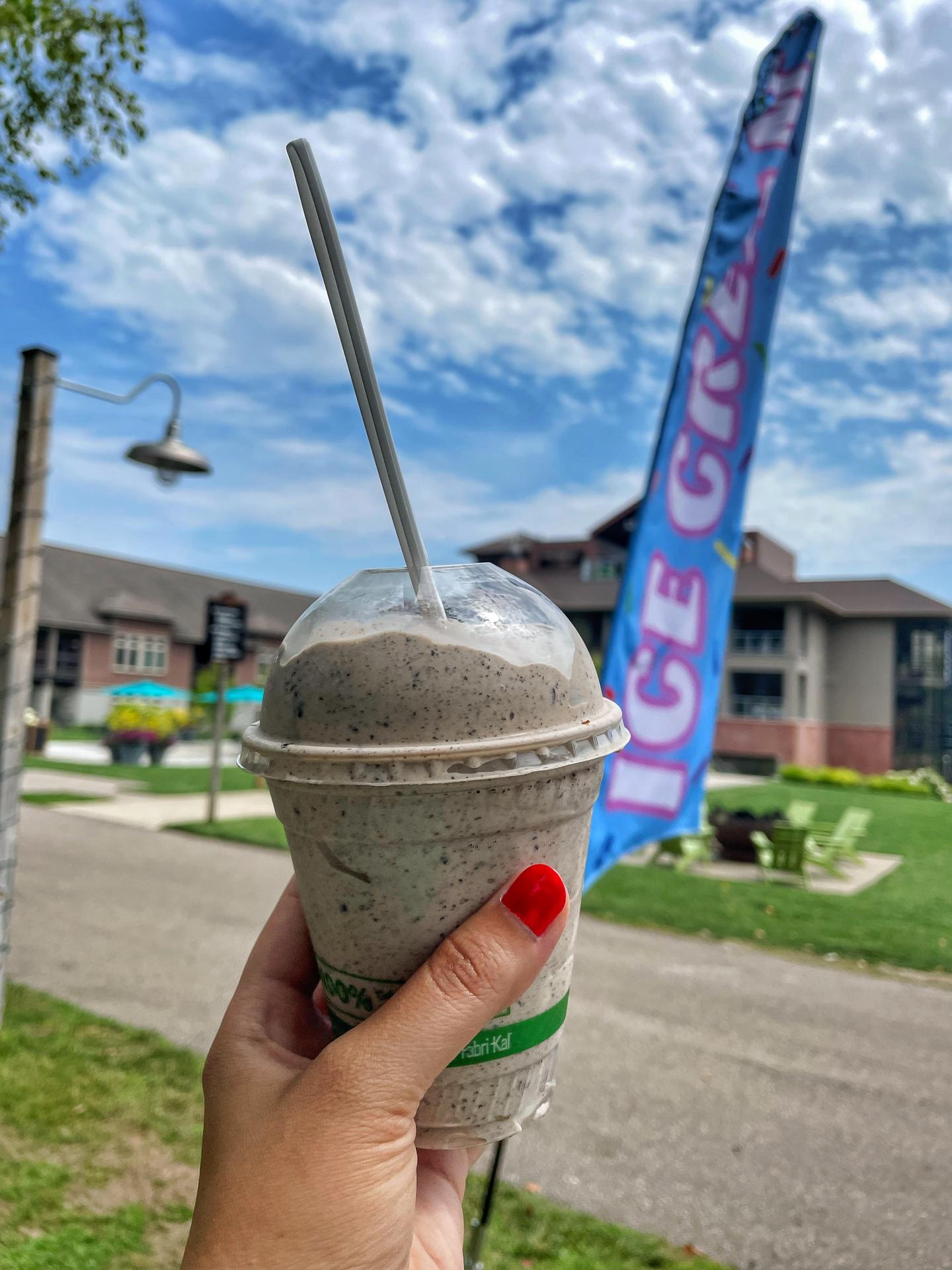 Milkshake in hand with colorful flag and buildings in the background.